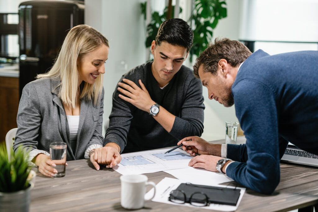 Real estate agent reviewing transfer paperwork with home buyers at a table, showing how an assumable mortgage transfers an existing rate.